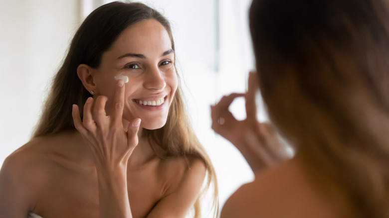 Woman applying face cream in mirror