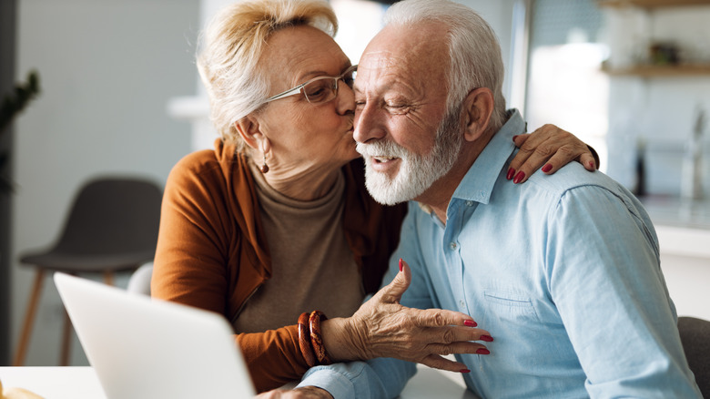 older woman kissing older man looking at computer