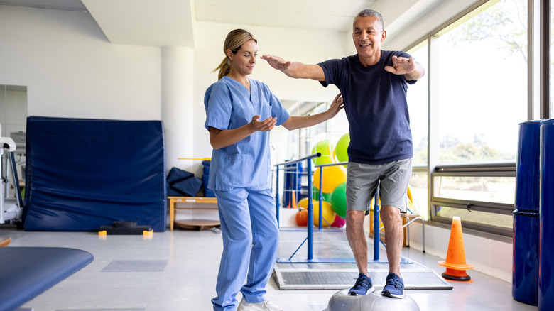 man balancing on a Bosu ball while working with a physical therapist