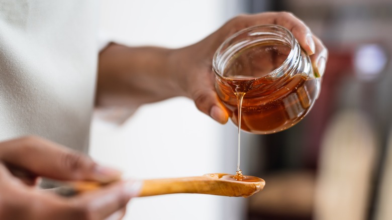Woman pouring honey from jar onto spoon