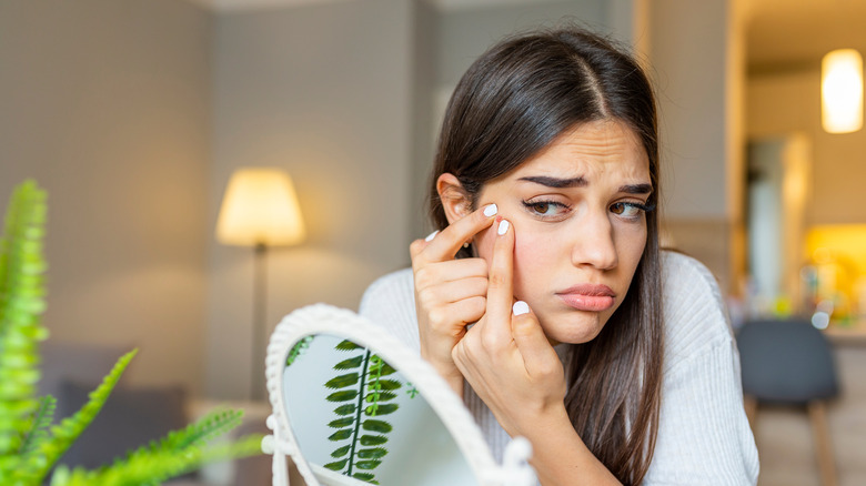 woman popping pimple on face