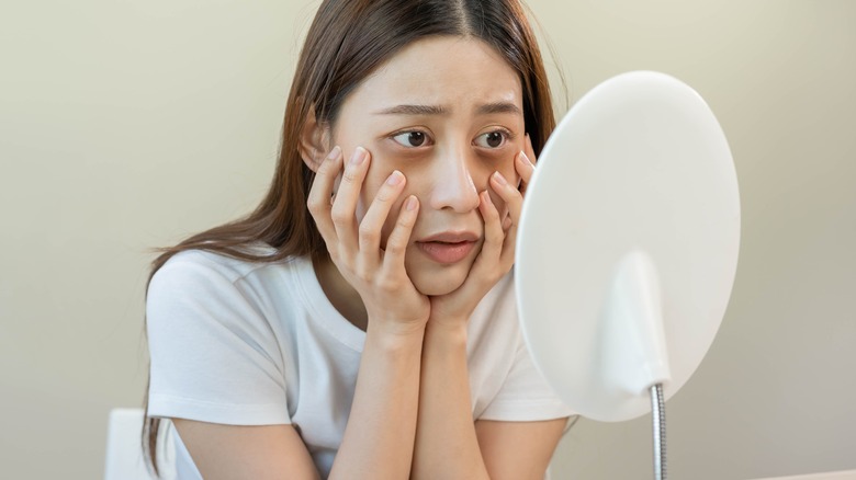 woman with dark circles look into mirror