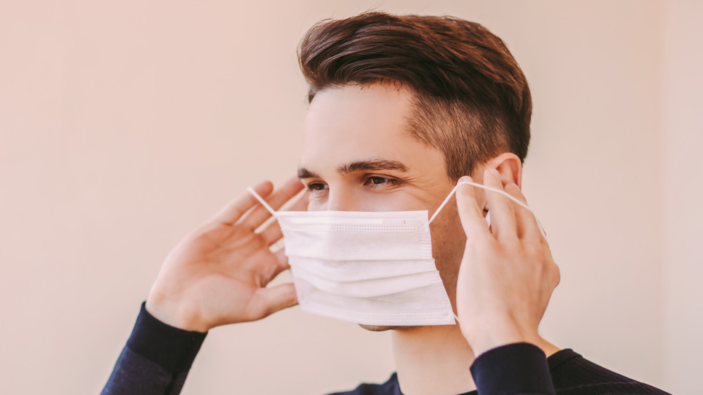 Person with short brown hair and dark shirt putting on a white surgical mask