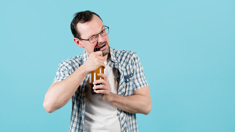 middle aged man opening a beer bottle with his teeth 