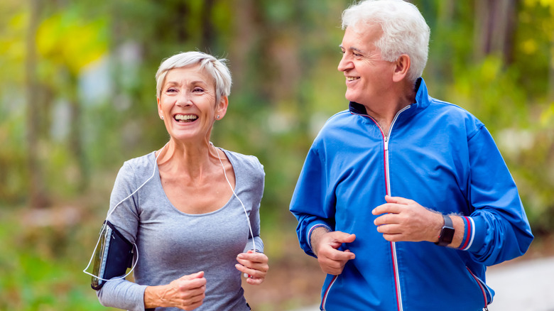 Smiling senior couple jogs through a park