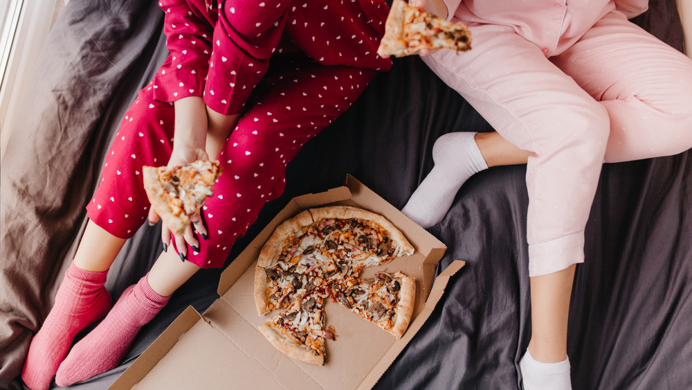 Two pajama clad girls women sharing a pizza in bed 