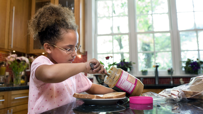 Young girl scooping peanut butter out of jar