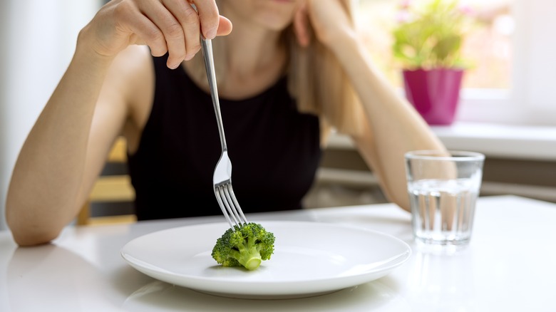 a woman has just a piece of broccoli on otherwise empty plate
