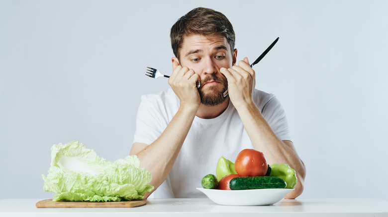 man looking at sparse veggies in front of him