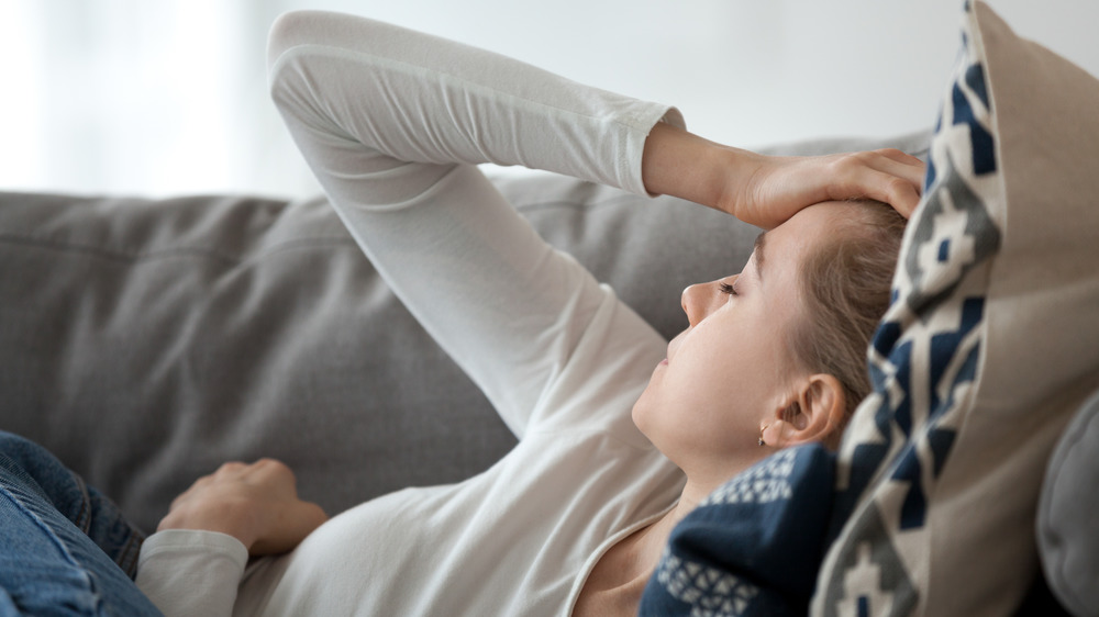 Woman lying on couch with hand on head in pain