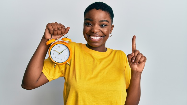 a young woman holding a clock and smiling