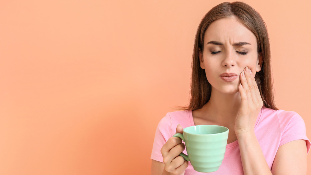 Person in pink shirt holding a green mug and grimacing while holding her mouth