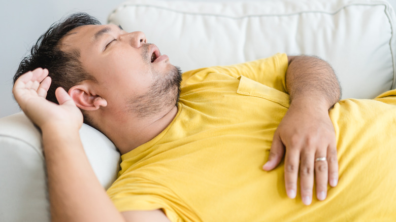 Man in yellow shirt asleep with open mouth on couch