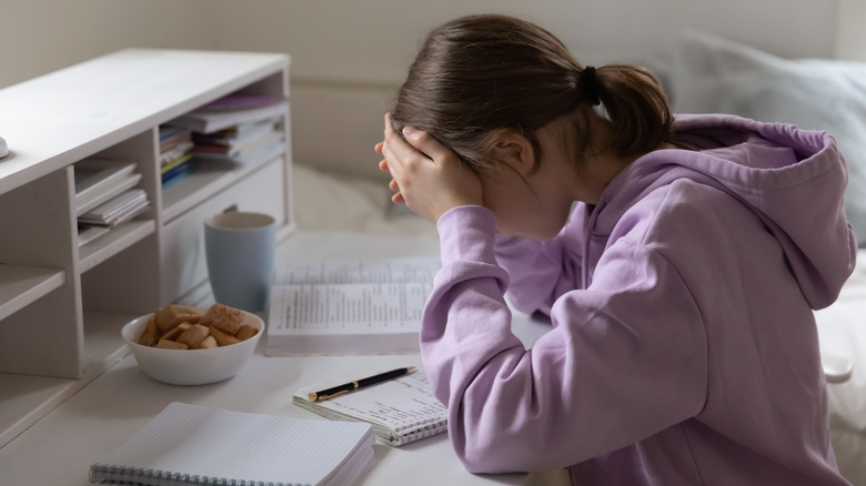 Young girl sits at desk with head in her hands