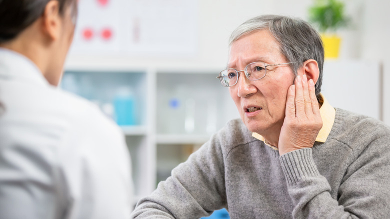 Patient touching painful ear talking with doctor