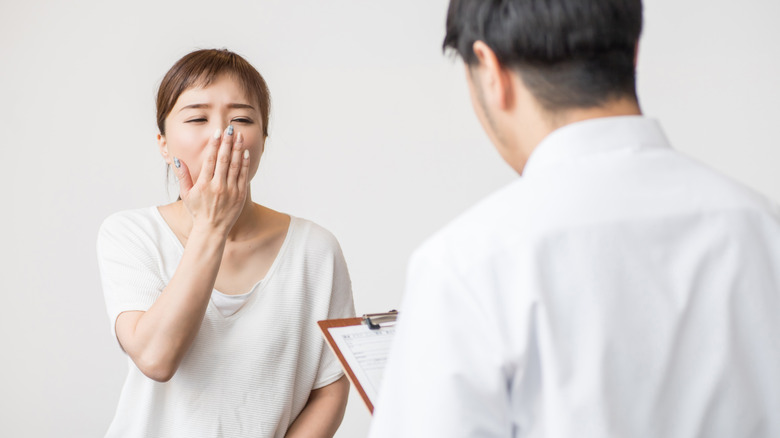 Woman covering her mouth while yawning and receiving consultation from doctor