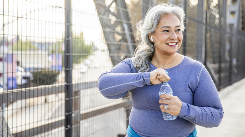 Smiling older woman opening water bottle