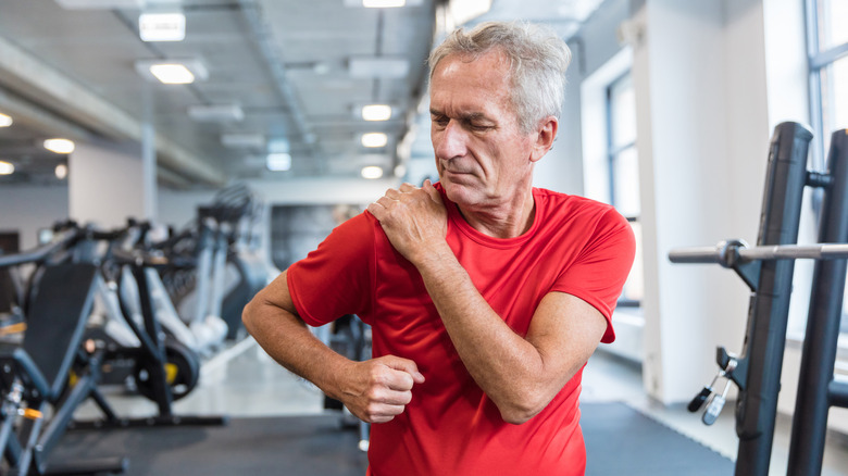 older man at the gym holding his sore shoulder