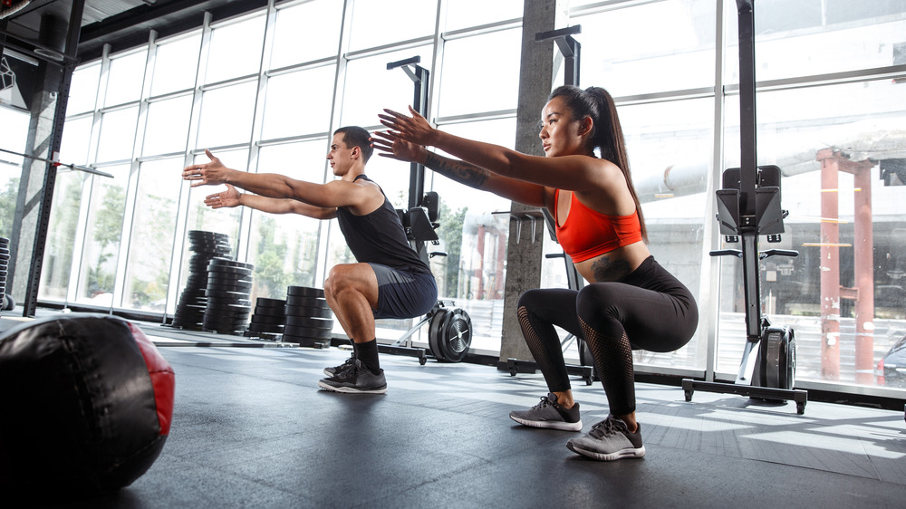 A man and a woman at the gym doing squats