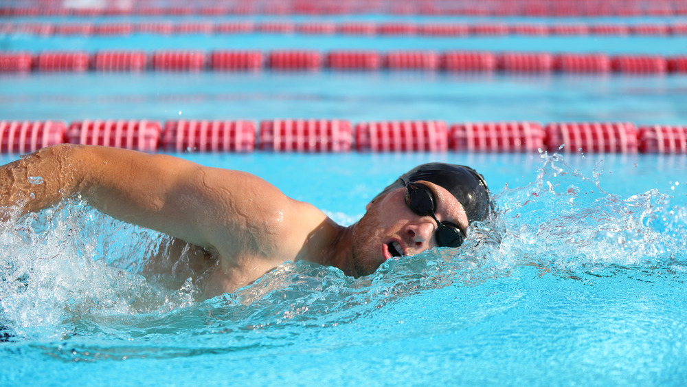 Man wearing a bathing cap and goggles while swimming in a pool