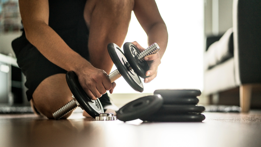 Close up of a man putting a weight plate on a dumbbell