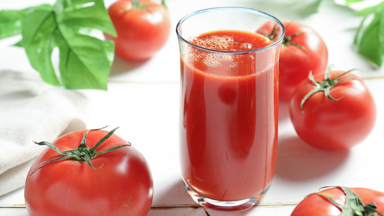 Glass of tomato juice by several tomatoes