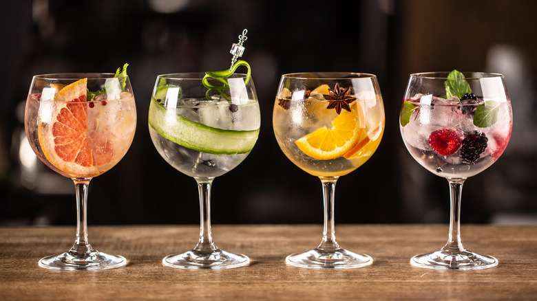 Four wine glasses filled with gin and tonic and different fruits and garnishes