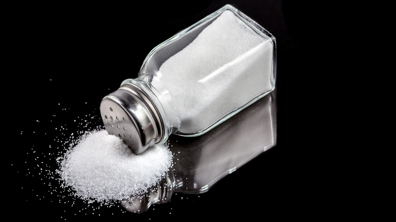 A salt shaker spilled out on its side against a black surface and background