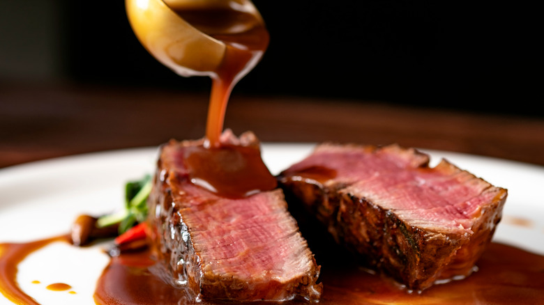 A ladle pouring demi-glace sauce over a medium rare grilled filet Mignon steak