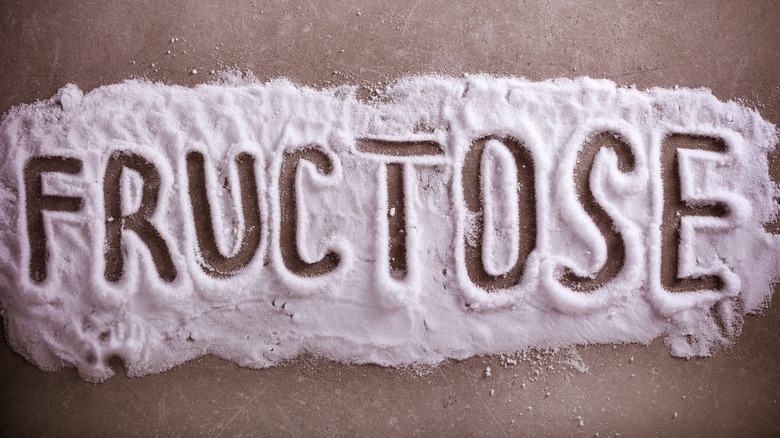 The word "fructose" written out in a pile of sugar against a brown background