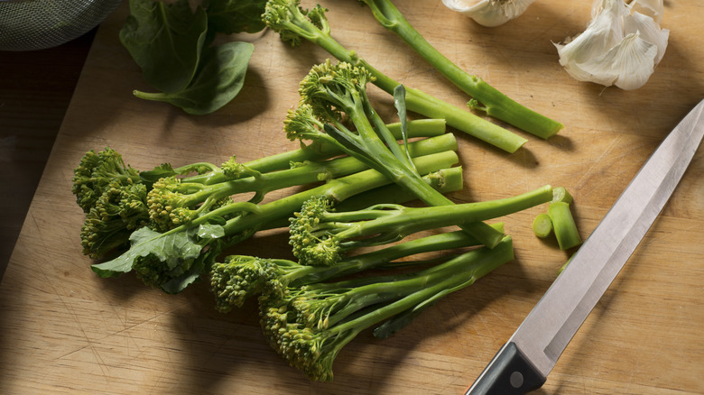 Broccoli stalks next to a knife on a wooden cutting board 