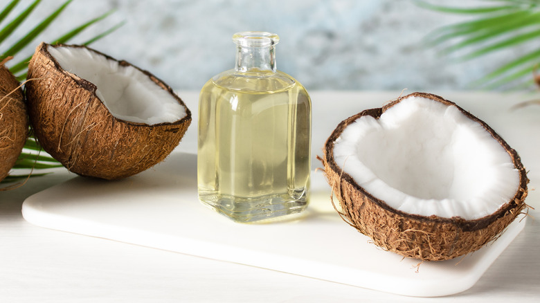 A bottle of coconut oil by fresh coconuts