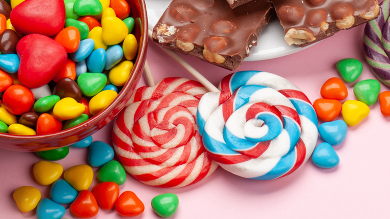 A bowl of candy next to a plate of chocolate bars, lollipops, and loose candies