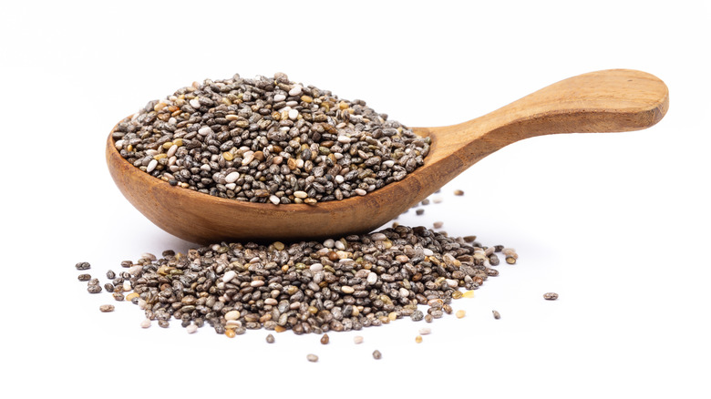 A wooden spoon filled with chia seeds next to a pile of chia seeds