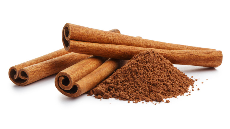 Three cinnamon sticks by a pile of cinnamon powder against a white background