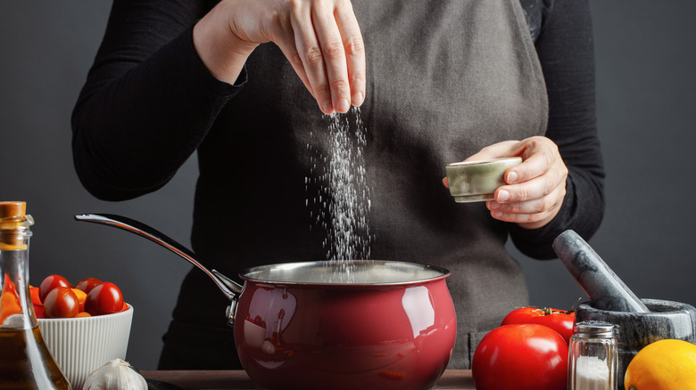 Woman sprinkling salt into a red pot 