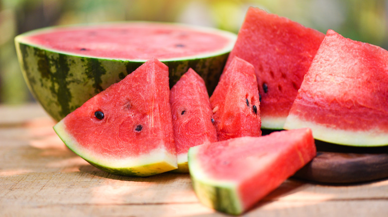 Slices of watermelon in front of and next to half a watermelon against a wooden surface