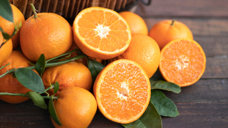 Whole and halved oranges piled in front of a basket with oranges