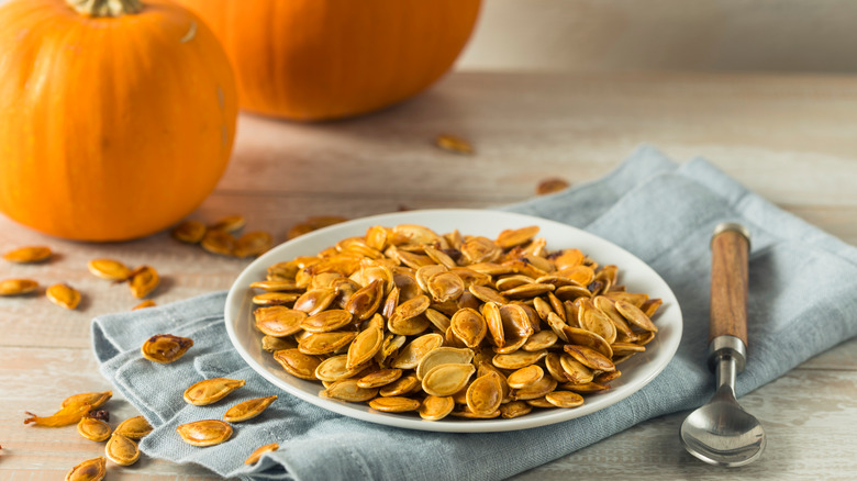 Home roasted pumpkin seeds on a white plate on a napkin with two pumpkins in the background