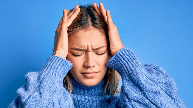 Woman in a large blue sweater holding her head with both hands