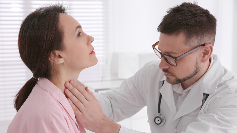 A doctor wearing glasses and examining a woman's throat 