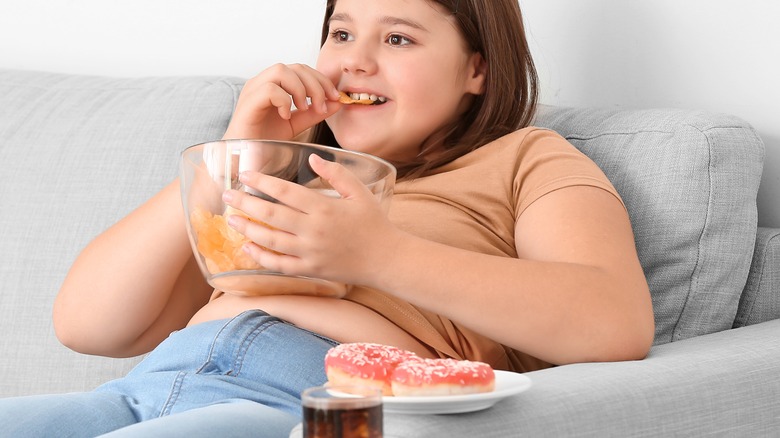 overweight girl on the couch eating unhealthy snack