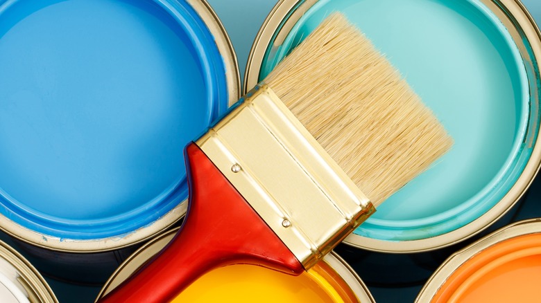 multiple colored paint gallons with a paint brush set on top