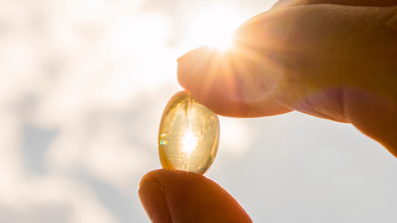 up close hand holding vitamin d capsule towards the sun