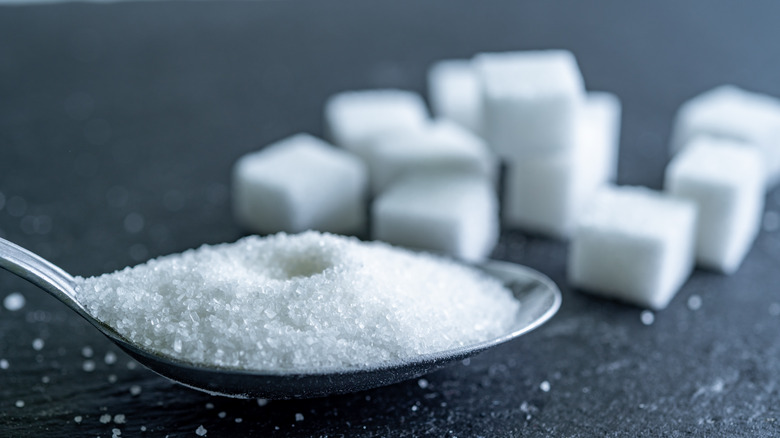 A spoon filled with sugar in front of sugar cubes against a dark gray background
