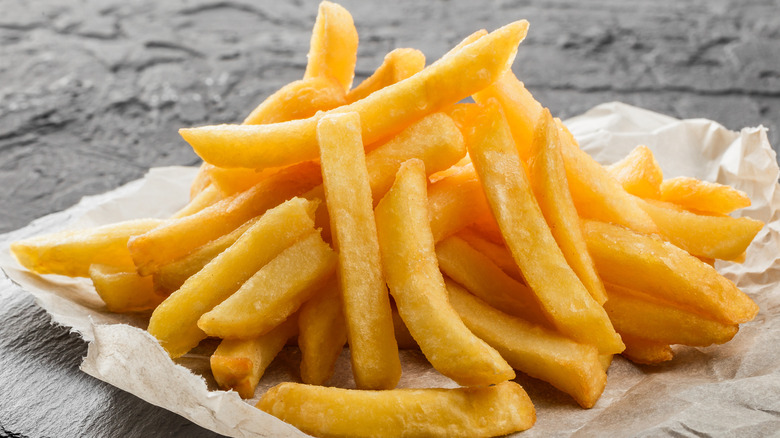 A pile of French fries on a paper towel against a gray stone and a gray surface