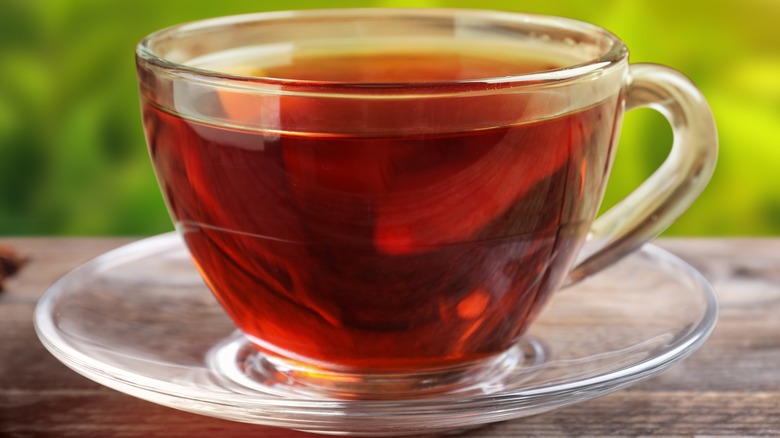 Steaming rooibos tea in a clear tea cup on a clear saucer against an out of focus outdoor background