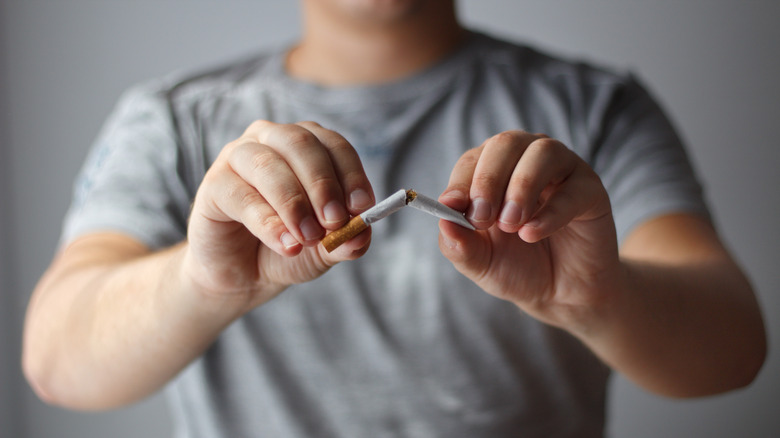Man in gray shirt against a gray background breaking a cigarette in half