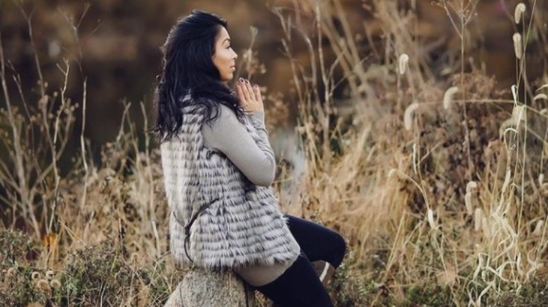 Thara sits on a rock with her hands in prayer 