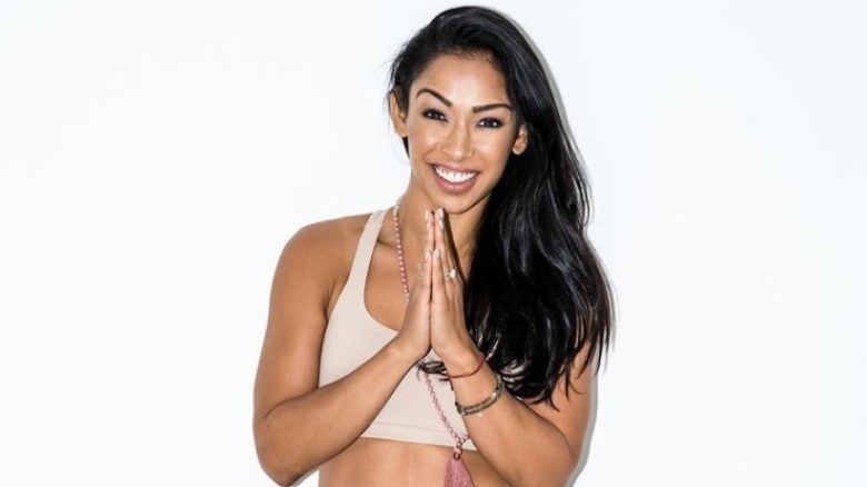 Thara stands in front of a white wall with her hands in prayer